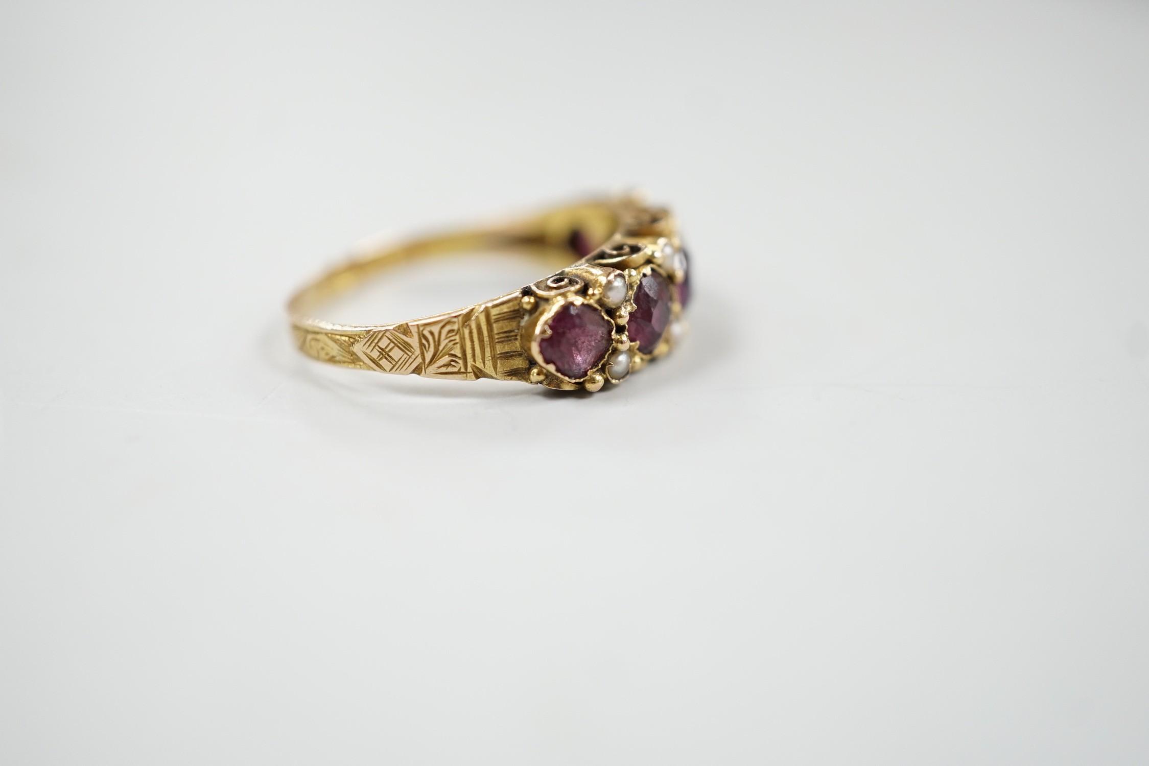 A late Victorian 15ct gold and graduated five stone garnet set half hoop ring, with split pearl spacers, size, P/Q, gross weight 2.5 grams.